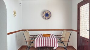 A dining area with a table covered by a striped tablecloth, four chairs, a decorative plate on the wall, and a wooden ceiling beam. - Cozy house in a picturesque white mountain village (Canillas de Albaida)