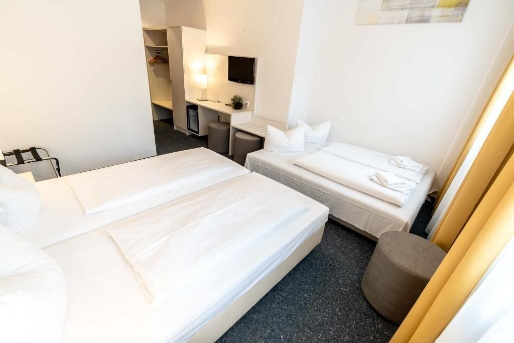 A hotel room with two beds, a desk with a chair, a television, and a small stool.