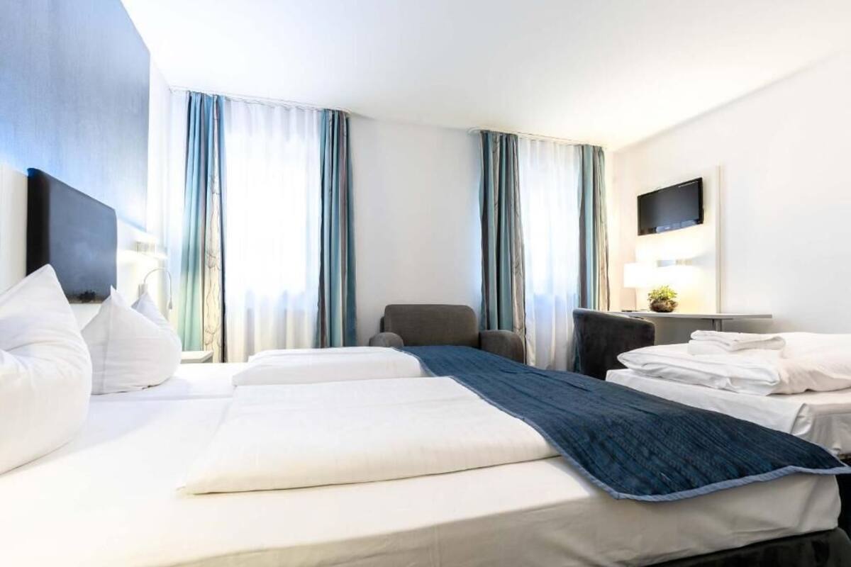 A hotel room with two beds, a desk, a chair, and a TV.