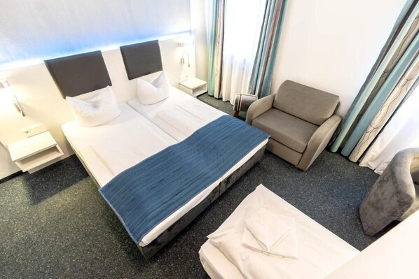 Una habitación de hotel con una cama grande, un sofá pequeño, una mesita de noche y cortinas.