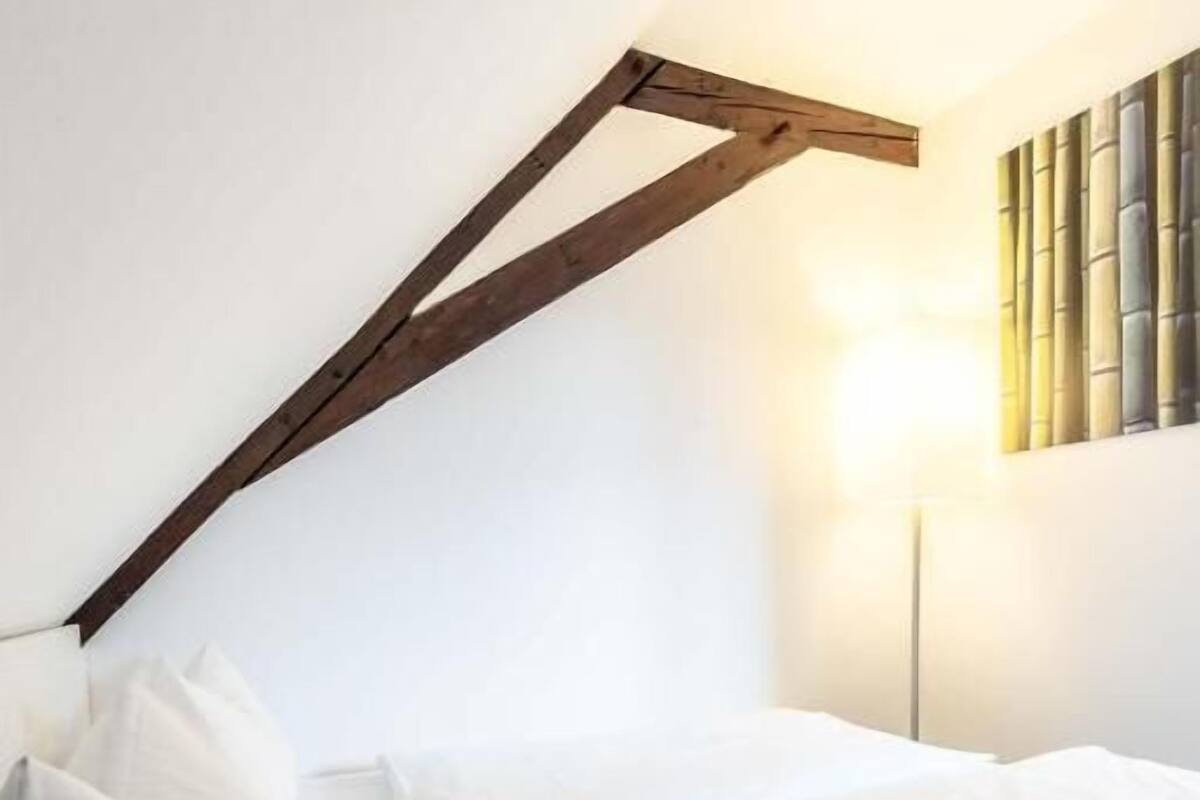 A bedroom with a sloped ceiling, a bed with white bedding, and a wall-mounted lamp.