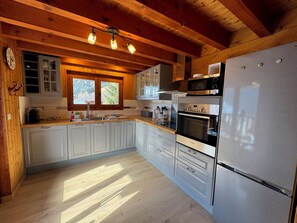 Une cuisine moderne avec des poutres en bois, un réfrigérateur en acier inoxydable et une fenêtre donnant sur un paysage pittoresque.