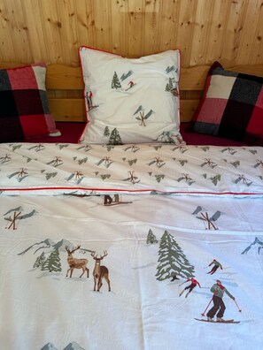 A bed with a white duvet featuring a winter sports theme, flanked by two pillows with a checkered pattern. - Stunning Alpine chalet for seven people with breathtaking mountain views! (La Chapelle-d'Abondance)