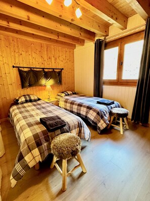 Een houten kamer met twee bedden, een bankje, een lamp en een raam.