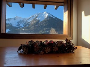 Een raam met uitzicht op een met sneeuw bedekte berg en een houten tafel met een decoratieve opstelling.