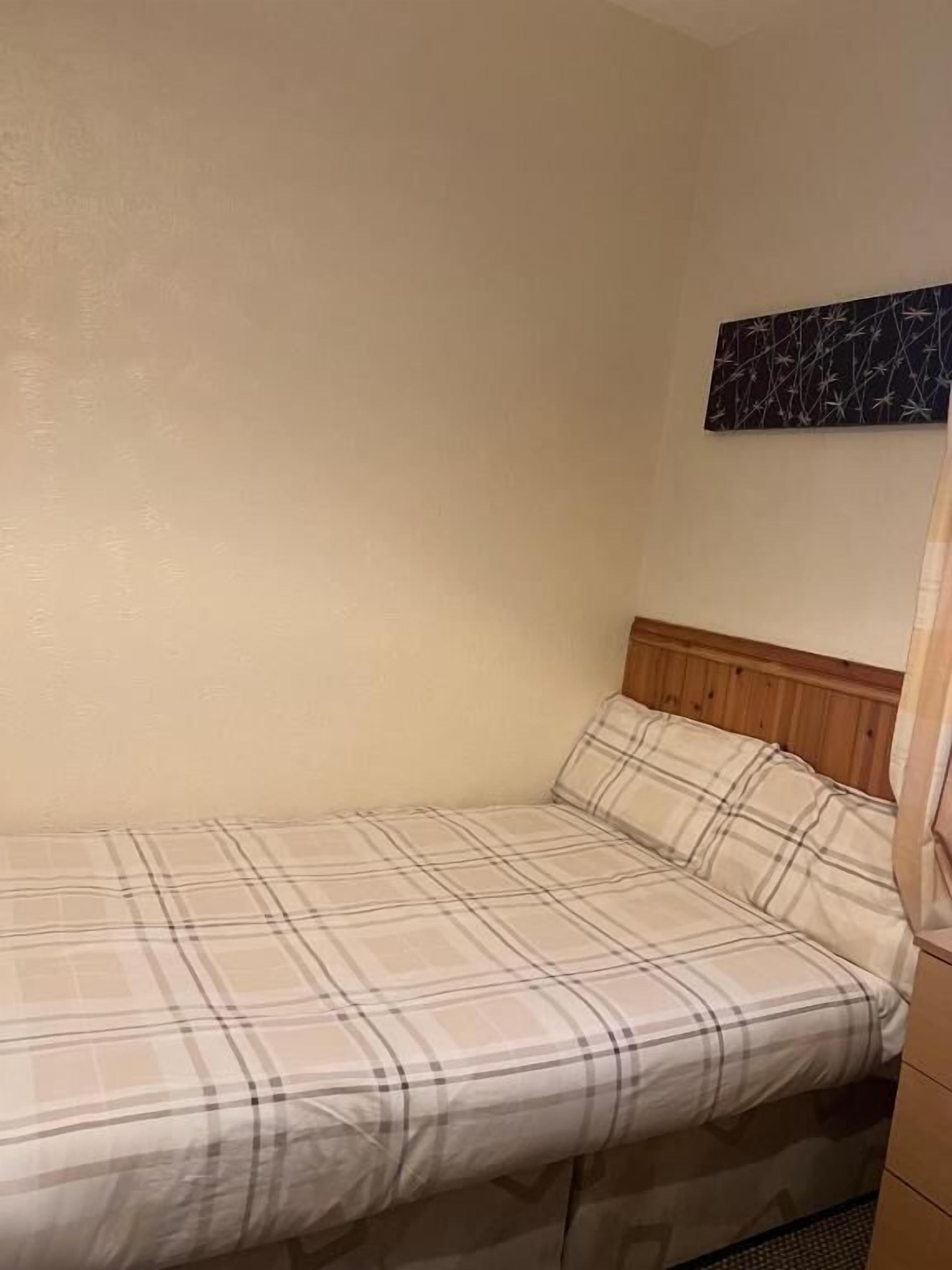 A single bed with a plaid bedspread in a room with a wooden headboard and a wall-mounted artwork.