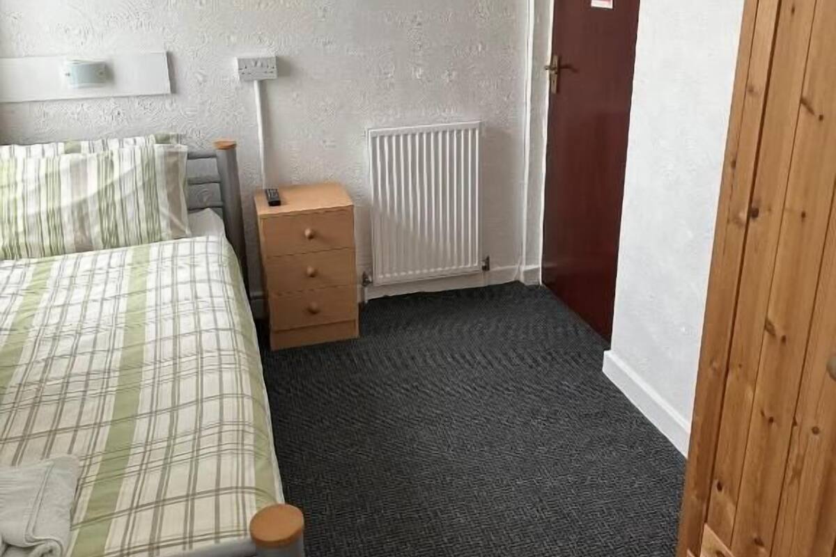 Een slaapkamer met een bed, een dressoir, een radiator en een kledingkast.