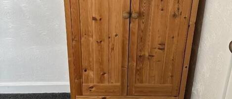 Un armario de madera con dos puertas y un estante inferior, frente a una pared con textura.