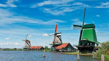 Three windmills with red roofs and green upper structures, situated by a body of water.