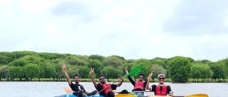 Eine Gruppe von Menschen paddelt mit Kajaks auf einem ruhigen Fluss, im Hintergrund sind Bäume zu sehen.