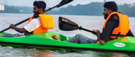Two people in a green kayak with life jackets, paddling on a body of water.