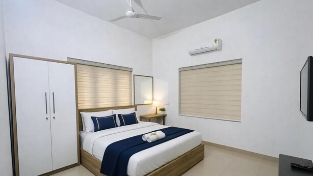 A bedroom with a bed, wardrobe, bedside table, lamp, air conditioning unit, and a TV. - Easy Nest Residency (Kannur)