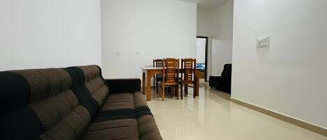 A living room with a sofa, a dining table with chairs, a ceiling fan, and a door leading to another room.