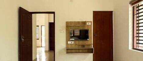 A room with a bed, a ceiling fan, a TV mounted on the wall, and a window with blinds.