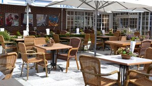 An outdoor cafe with wicker furniture, white umbrellas, and a brick wall with artwork. - Family-Friendly Getaway | Near Scenic Dunes, Nature Sites, and Outdoor Trails (Bergen)