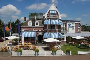 Un hotel con toldo a cuadros, mesas al aire libre y un jardín.