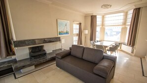 A modern living room with a sofa, a fireplace, a dining area, and large windows. - Family-Friendly Getaway | Near Scenic Dunes, Nature Sites, and Outdoor Trails (Bergen)