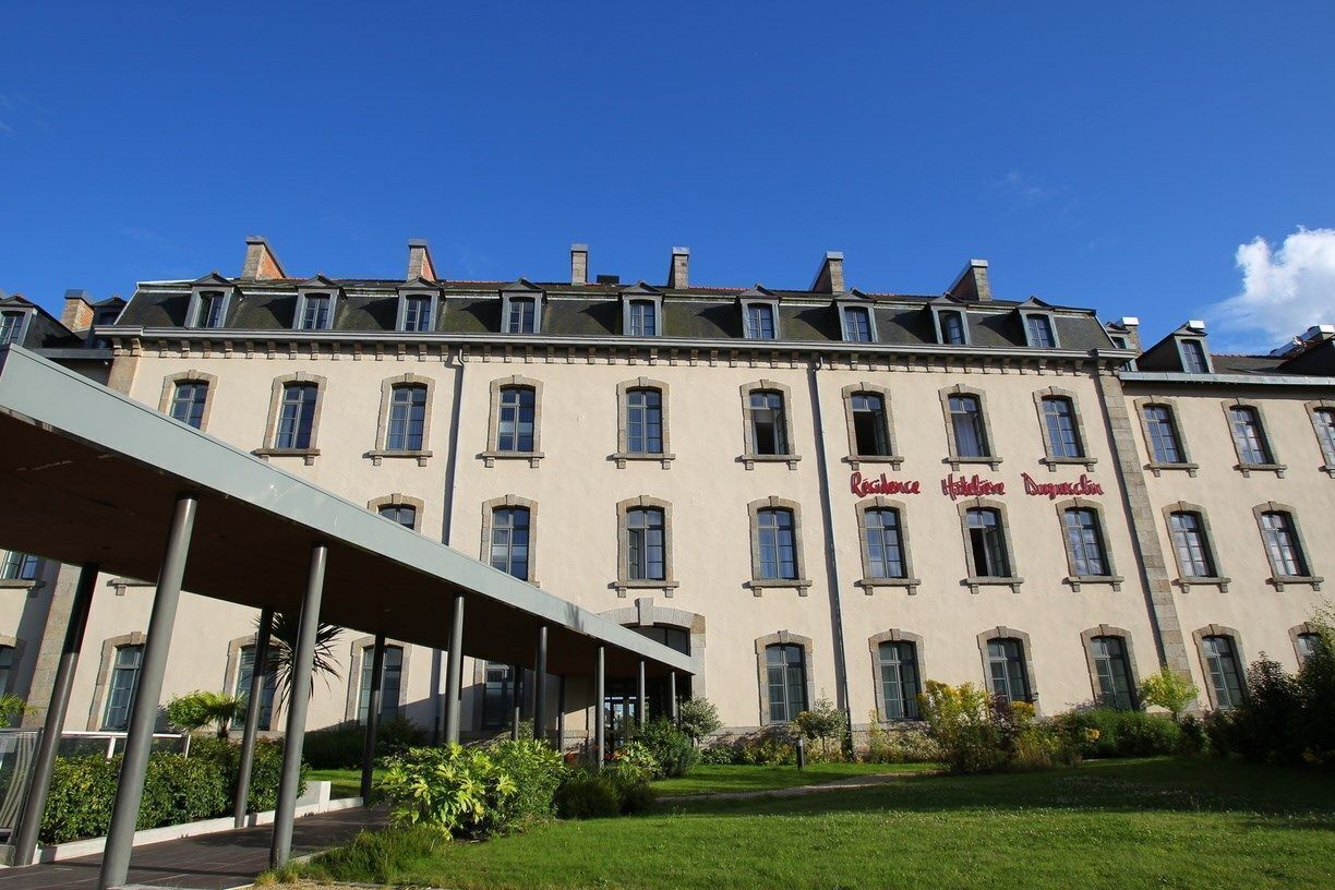 Un grand immeuble à étages, de style architectural classique, doté d’une entrée centrale et d’une allée couverte.