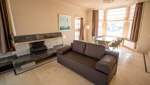 Een moderne woonkamer met een bank, een open haard, een eethoek en een groot raam met gordijnen.