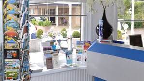 Ein Empfangsbereich mit einer gestreiften blauen und weißen Theke, einer weißen Vase mit weißen Blumen sowie einer Broschürenauslage mit Reiseangeboten.