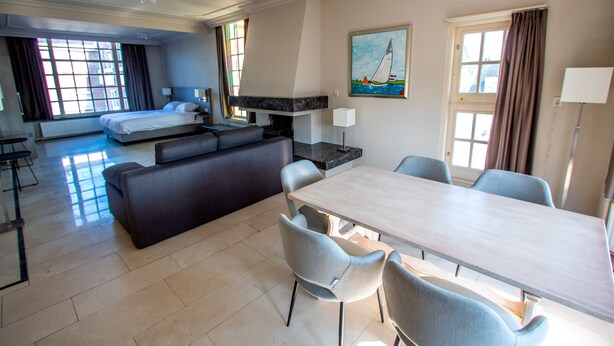 Ein Hotelzimmer mit Bett, einer Couch, einem Esstisch mit Stühlen, einem Kamin und einem Bild an der Wand.