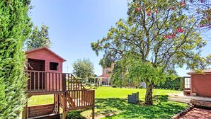 A residential area with a wooden deck, a small red building, and a tree with red flowers.