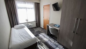 Ein Hotelzimmer mit Bett, Schreibtisch, Stuhl, Kleiderschrank, Fernseher und einem Fenster mit Vorhängen.