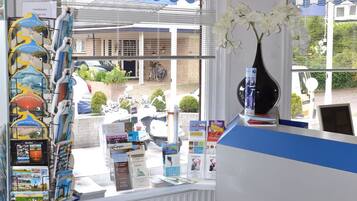 Ein Empfangsbereich mit einer gestreiften blauen und weißen Theke, einer weißen Vase mit weißen Blumen sowie einer Broschürenauslage mit Reiseangeboten.
