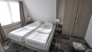 Une chambre d’hôtel avec un lit double, deux tables de chevet avec des lampes, une armoire et une fenêtre avec des rideaux.