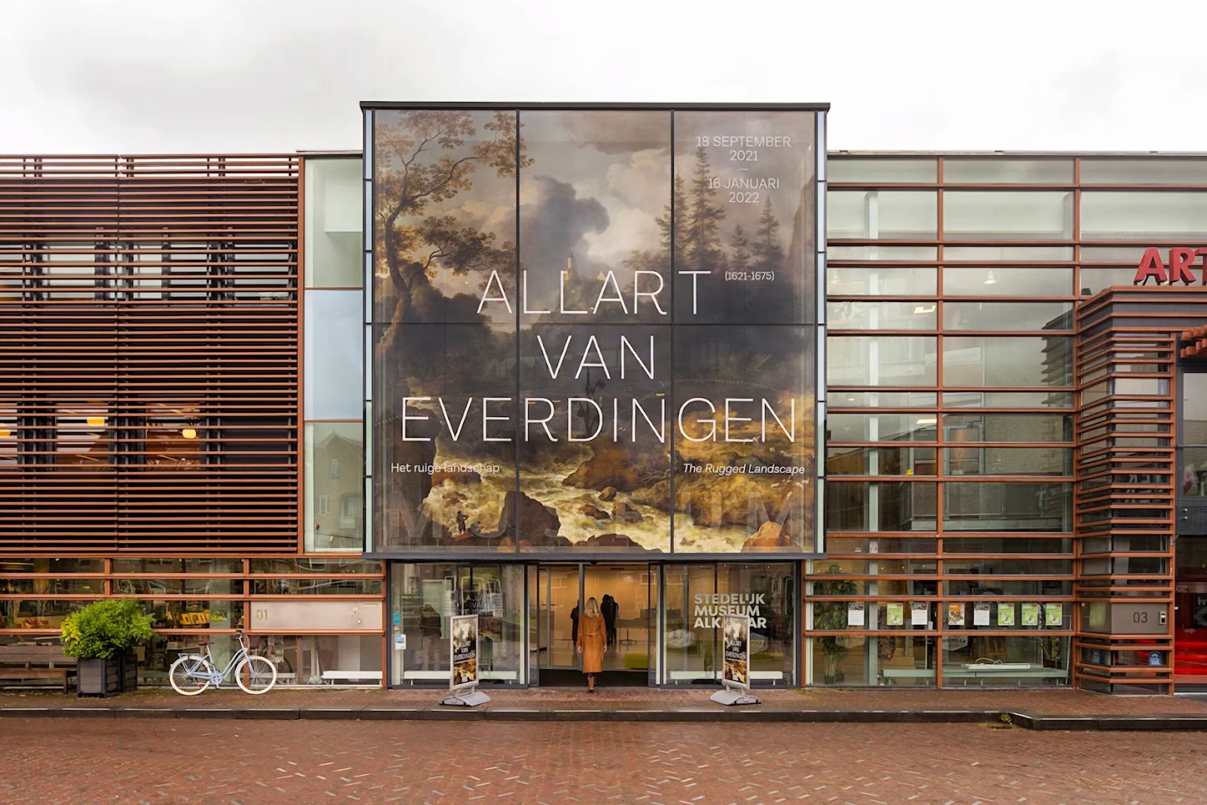 Een gebouw met een groot reclamebord waarop 'Allart Van Everdingen' en 'Het Ruige Landschap' staan.