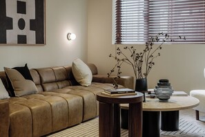 Ein modernes Wohnzimmer mit Ledersofa, rundem Couchtisch und einer Vase mit Zweigen.