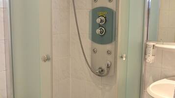 A glass-enclosed shower with a control panel, a toilet, and a sink.