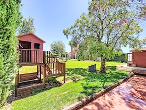 Un quartier résidentiel avec une terrasse en bois, un petit bâtiment rouge et un arbre aux fleurs rouges.