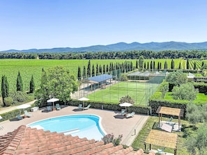 A swimming pool, sun loungers, and a tennis court surrounded by greenery and mountains.