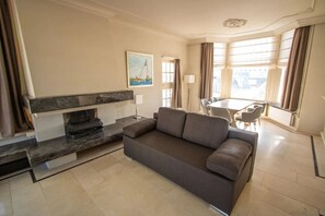 En moderne stue med sofa, pejs, spiseplads og store vinduer.