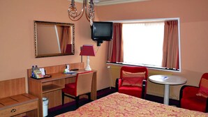 Habitación de hotel con cama, escritorio, silla, televisión y ventana con cortinas.
