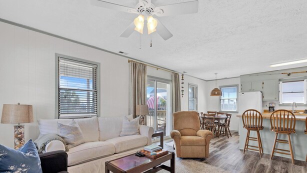 A living room with a sofa, armchair, coffee table, and a dining area with chairs and a table. - Spread'N Kindness | Pet-Friendly + One Block from the Beach (Surf City)