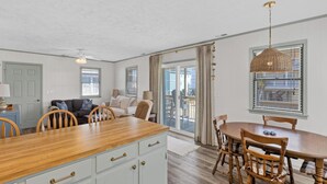 A kitchen with a wooden island, white cabinets, and a dining area with wooden chairs and a table. - Spread'N Kindness | Pet-Friendly + One Block from the Beach (Surf City)