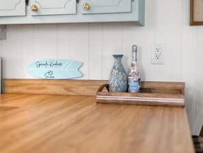 Un comptoir de cuisine en bois, agrémenté d’une enseigne décorative, d’un vase et d’une bouteille.