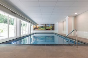 An indoor swimming pool with a view of a landscaped area outside, a mural on the wall, and a metal handrail. - Your Relaxing Base for Outdoor and City Adventures! Indoor Pool, Onsite Dining! (Berg en Dal)