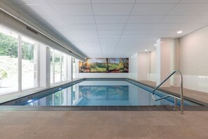 An indoor swimming pool with a view of a landscaped area outside, a mural on the wall, and a metal handrail. - Charming Woodland Stay with Free Parking and Indoor Pool, Near Valkhof Museum! (Berg en Dal)