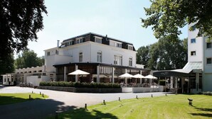 A two-story building with a restaurant named 'RESTAURANT DI VILLA' and a hotel named 'HOTELFICCA' with outdoor seating and umbrellas. - Relax and Recharge! Indoor Pool and Parking, Just Minutes from Grote Markt! (Berg en Dal)