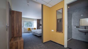 A hotel room with a bed, a desk, a chair, a window, and a bathroom with a sink and mirror. - Relax and Recharge! Indoor Pool and Parking, Just Minutes from Grote Markt! (Berg en Dal)