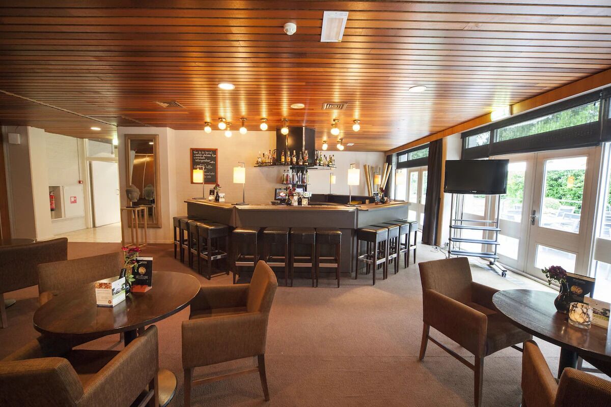 A bar area with a counter, stools, and a television screen. There are tables with chairs in the foreground.