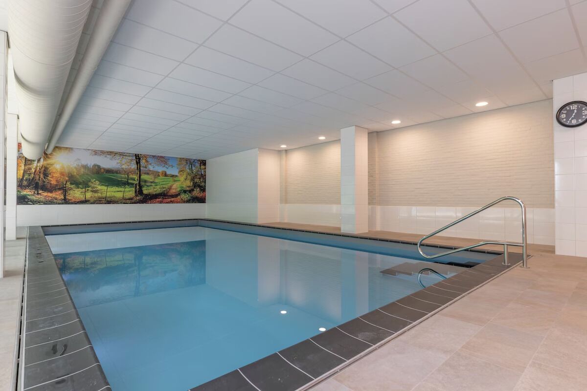 A swimming pool with a tiled border, a mural on the wall, and a clock on the wall.