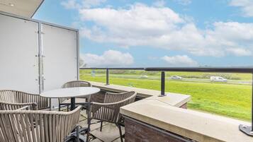 A balcony with wicker chairs and a table, overlooking a highway with passing vehicles.