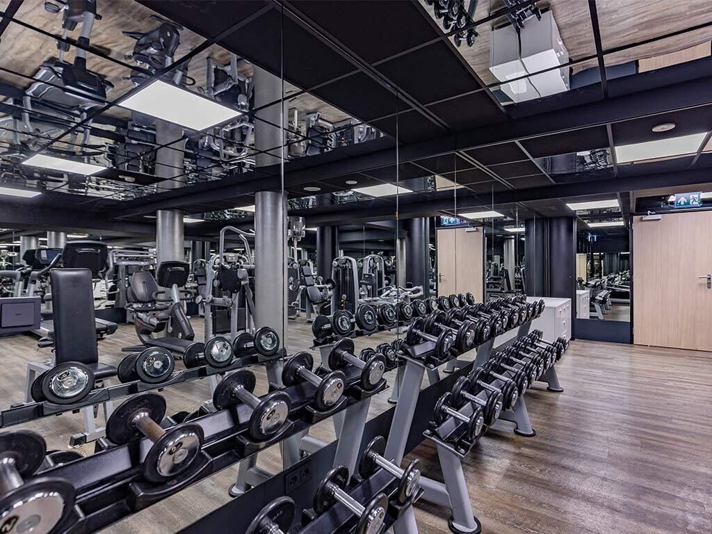 Et fitnesscenter med rækker af håndvægte, træningsmaskiner og spejle på væggene.