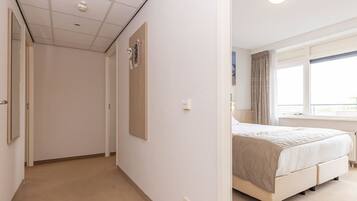 Une chambre d’hôtel avec un lit, une fenêtre avec des rideaux, une porte et un luminaire fixé au mur.