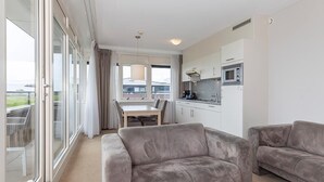 Un appartement moderne comprenant un coin repas, une cuisine et deux canapés gris.