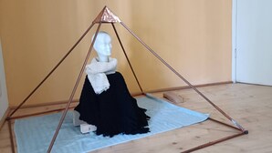 A mannequin in a black dress seated on a blue mat inside a tent-like structure with a wooden floor. - WEEKEND HEALTH WELLNESS REGENERATE (Bossico)